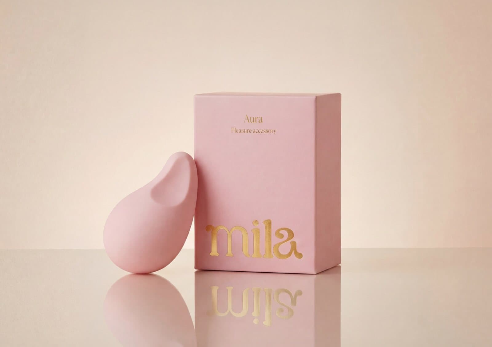 The pink Aura massager standing beside its pink gift box, lettered in gold.