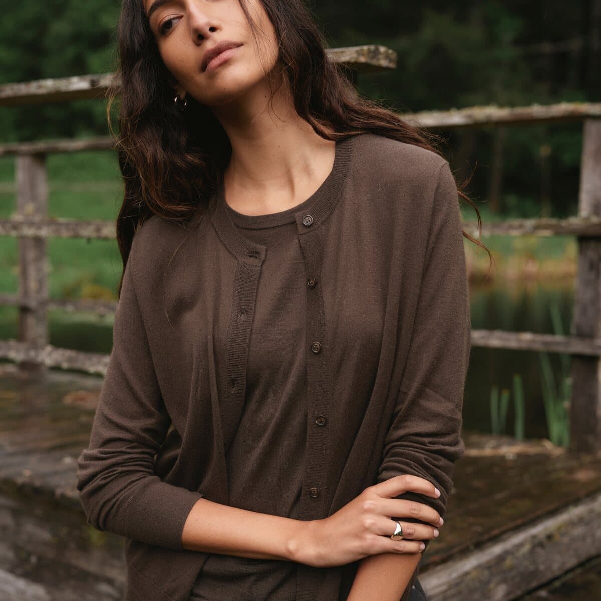 A woman wears the Jenni Kayne Monroe cardigan in deep truffle brown, buttoned at the neck.