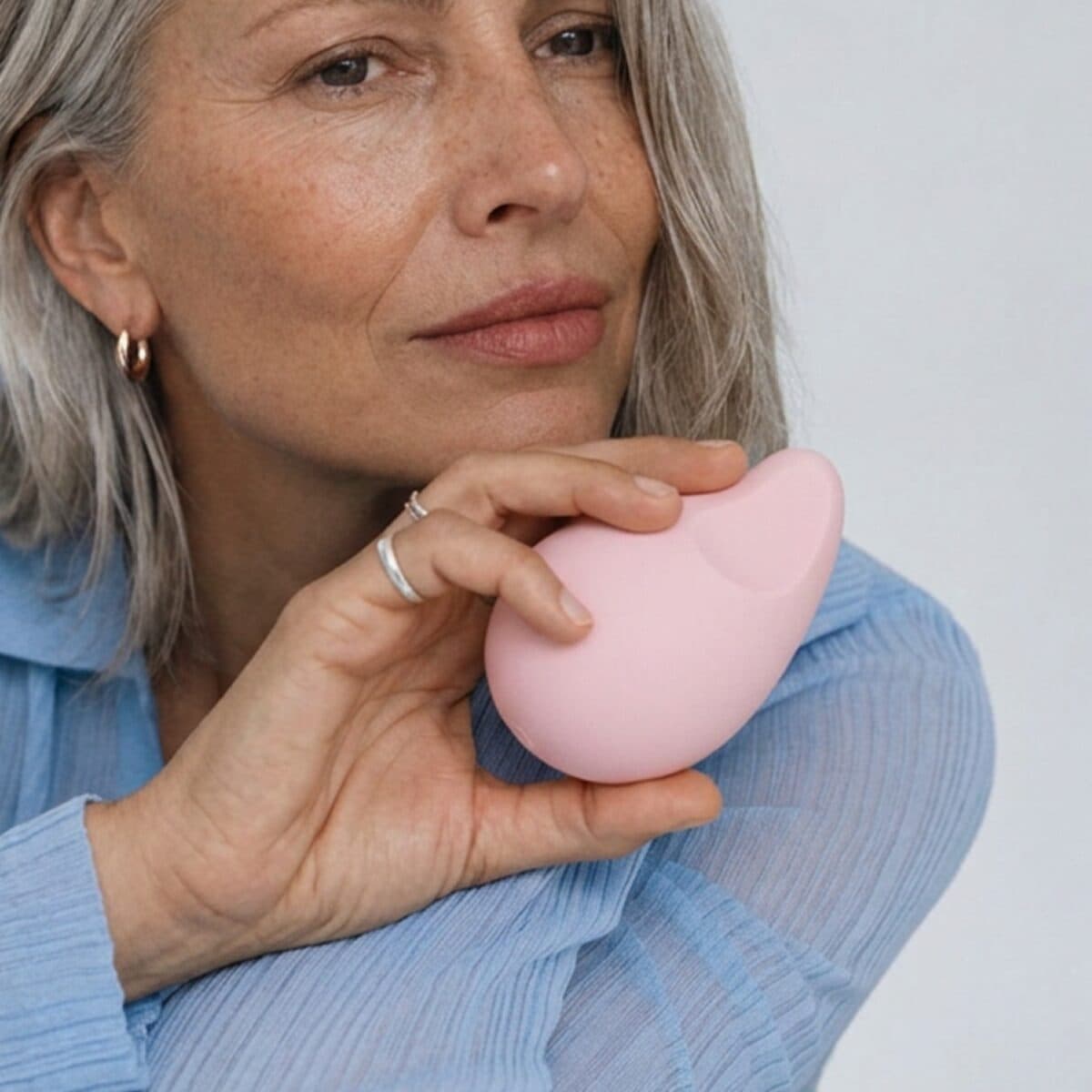 A woman holds the palm-sized pink Aura massager between her fingers.