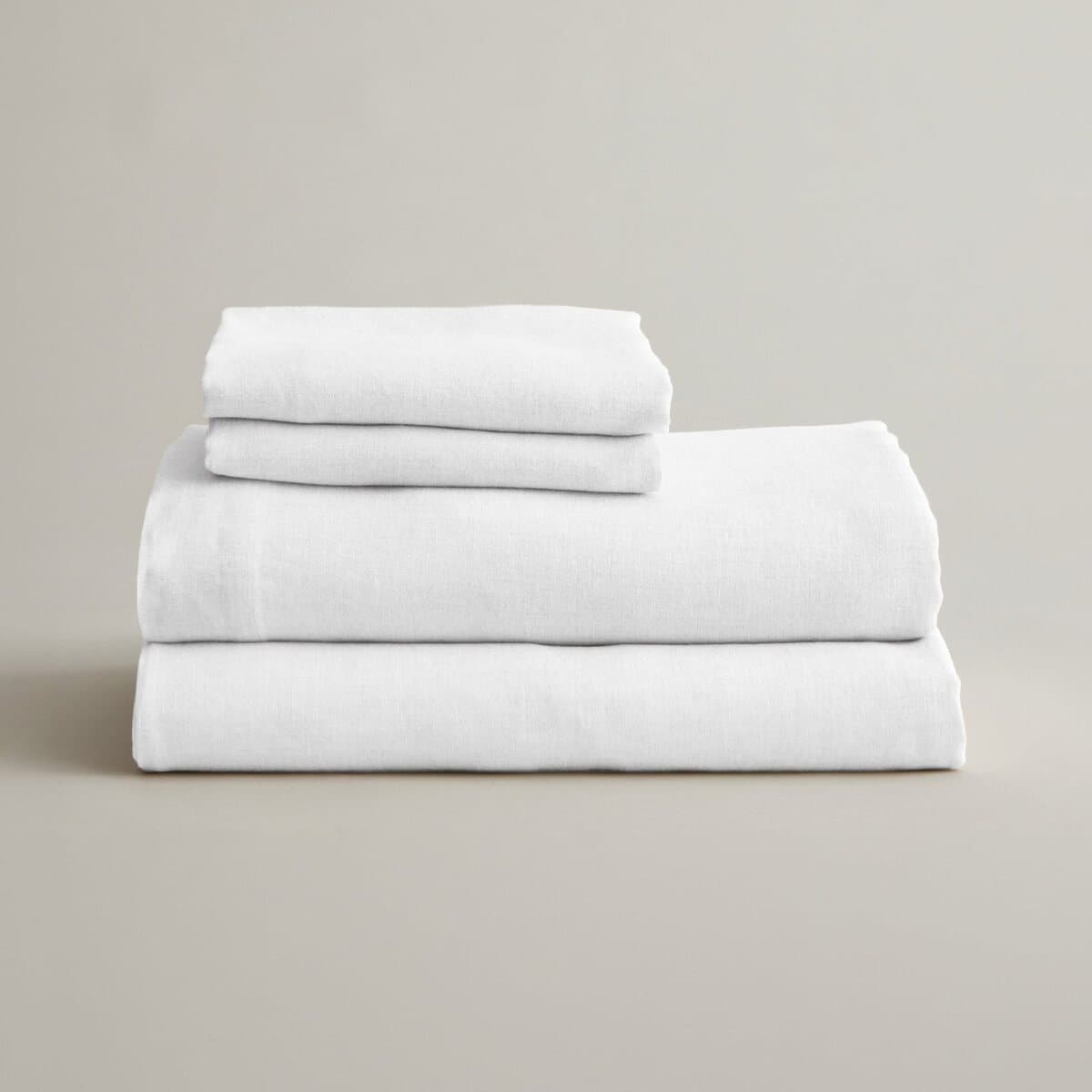 A folded stack of white CULTIVER linen sheets and pillowcases on a pale grey ground.
